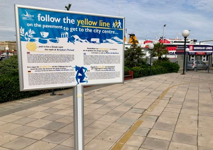 Línea amarilla pintada en la acera, cerca de un cartel que explica que conduce al centro de la ciudad de Heraklion.