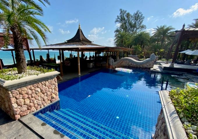 Bar de la piscina con techo tailandés junto a una piscina azul brillante frente al mar