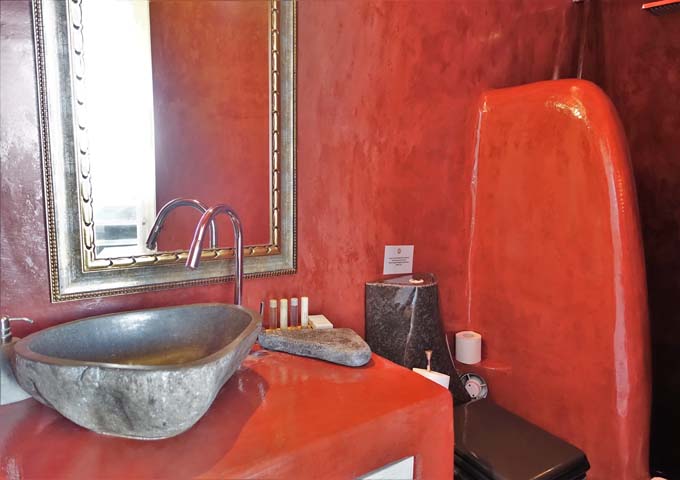 El baño de la villa de color rojo brillante tiene una ducha tipo cueva y lavabo de roca.