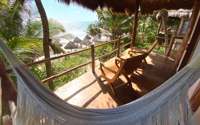 vista de sombrillas de paja y una playa bordeada de palmeras desde una hamaca en el balcón