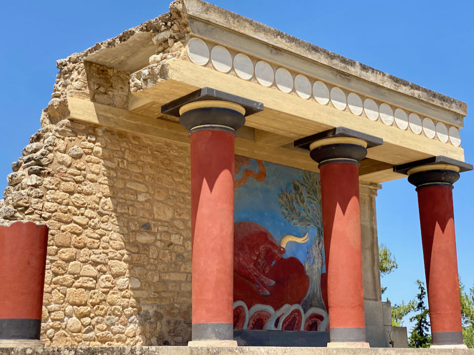 Antiguo edificio de piedra con pilares de color rojo brillante y una pintura de un toro.
