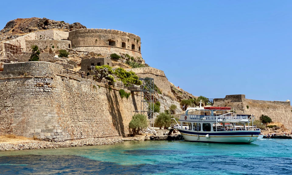 Un barco turístico amarrado en una imponente isla fortaleza veneciana en un día despejado.