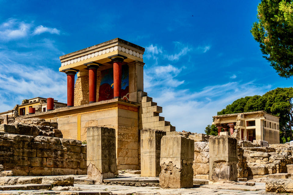 Foto de las ruinas del palacio de Knossos que muestra columnas pintadas de vivos colores y un fresco de toro