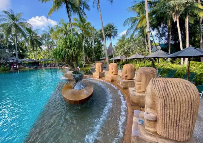 Hermosa piscina rodeada de estatuas y palmeras.